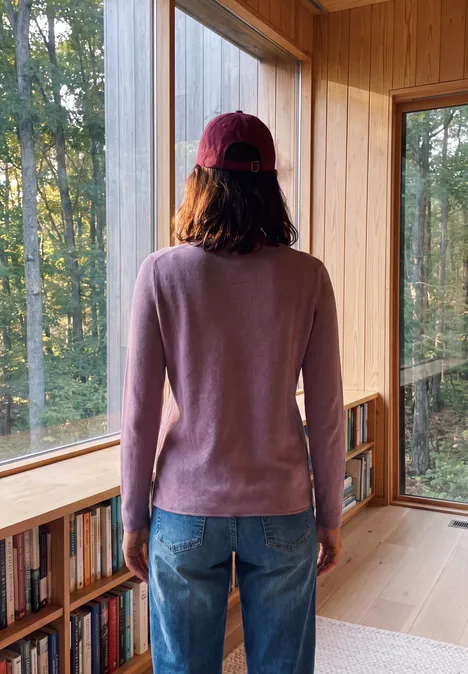 Personne en pull rose et jean, de dos, dans une pièce en bois lumineuse avec de grandes fenêtres.