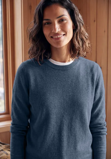 Femme souriante en pull bleu devant un mur en bois