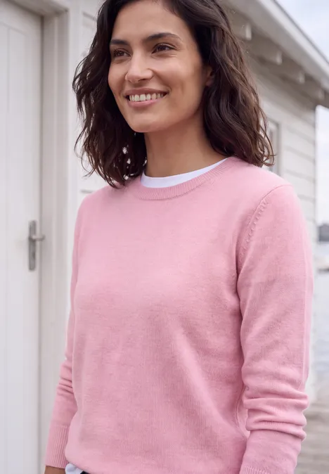Eine lächelnde Frau in einem rosa Pullover vor einer weißen Tür.