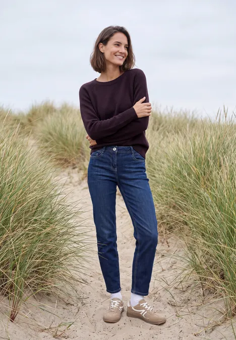 Pullover mit Rundhals und Strukturmix eggplant red melange Eine Frau in Jeans und Pullover geht lächelnd zwischen Dünen am Strand spazieren.