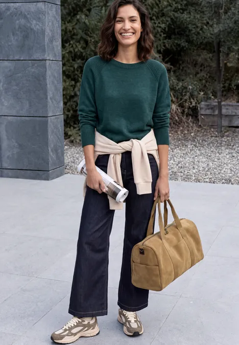 Trui met ronde hals en structuurmix dark sea green melange Frau mit grünem Pullover und Jeans steht vor einem Gebäude, trägt Sneakers und hält Tasche und Beutel.
