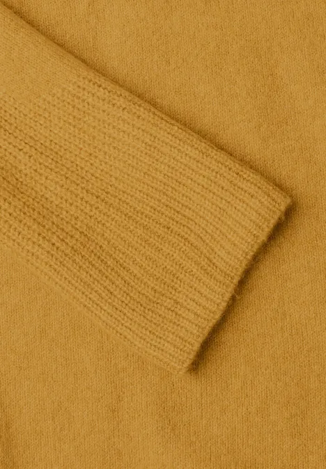 Nahaufnahme eines senfgelben Strickpullovers mit Ärmel und Körper in sanfter Textur.