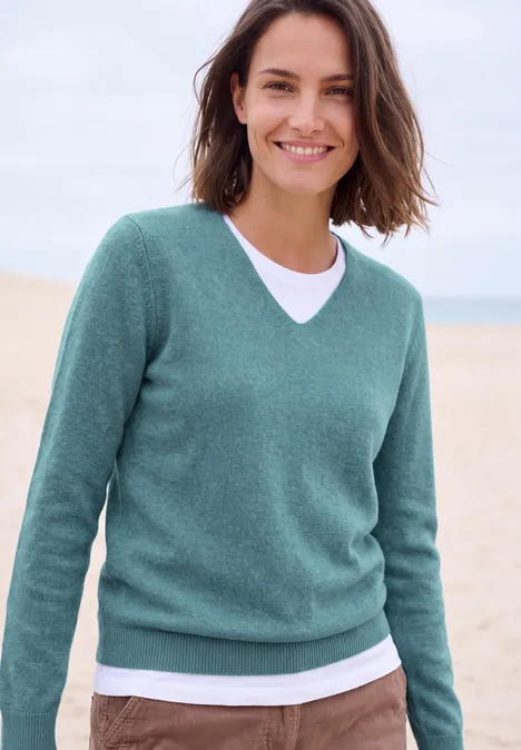 Lachende vrouw in groene trui en wit T-shirt op het strand.