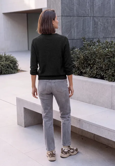 Pull col V à manches longues black melange Frau in schwarzem Pullover und grauer Hose steht vor modernem Gebäude.
