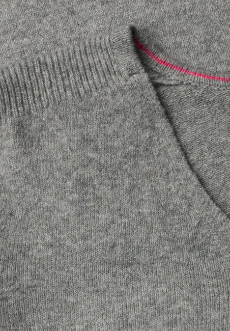 Close-up van een grijze gebreide trui met ronde hals, opgestikte zak en felroze stiksel.