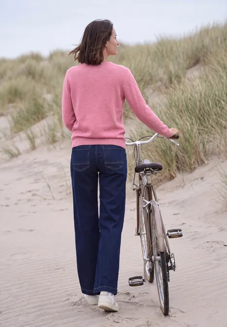Vrouw van achteren duwt fiets over zandduinen op het strand.