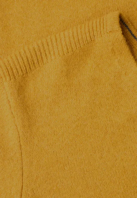 Nahaufnahme eines senffarbenen Strickpullovers mit Tasche und feiner Struktur.