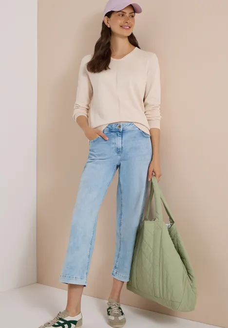 Frau in beigem Pullover, weitem Jeans, Basecap und grünem Stepp-Shopper