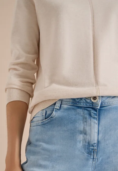 Beige Cardigan und blaue Jeans an einer stehenden Person, Fokus auf Taille und Oberkörper.