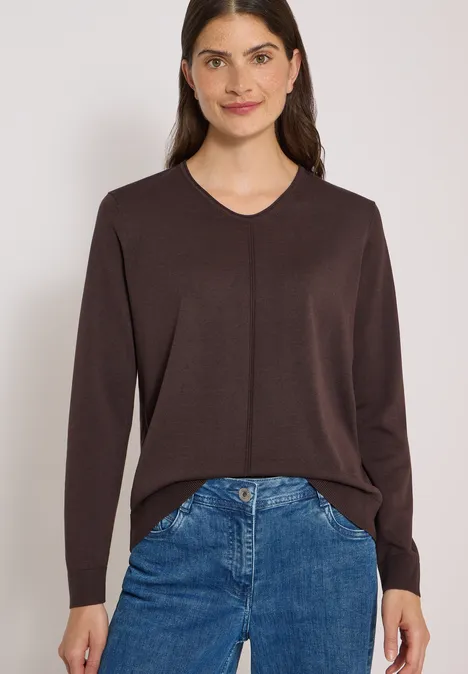 Frau in braunem V-Pullover und blauen Jeans.
