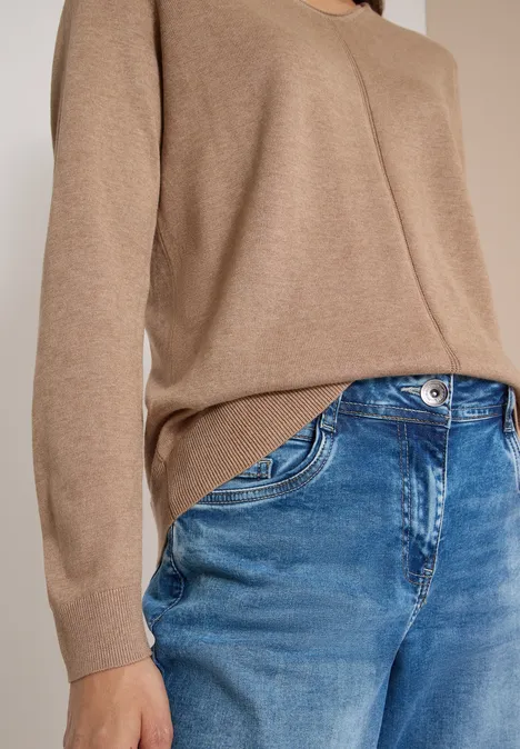 Nahaufnahme eines Oberkörpers in hellbraunem Pullover und blauen Jeans.