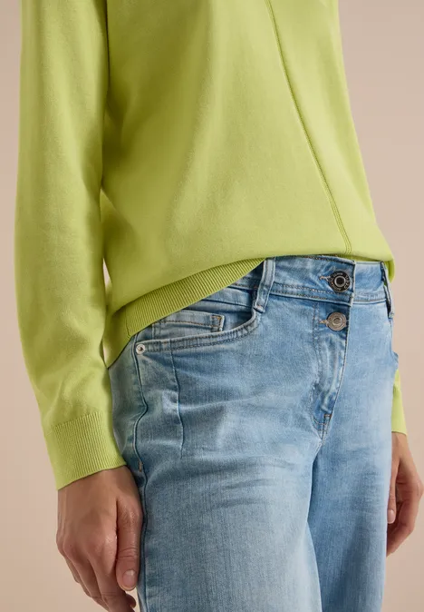 Person trägt hellgrünen Pullover und hellblaue Jeans, Bildausschnitt auf Torso und Arme.