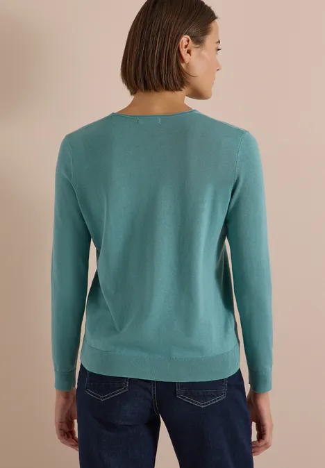 Rückenansicht einer Person in einem türkisfarbenen Langarmshirt und dunklen Jeans.