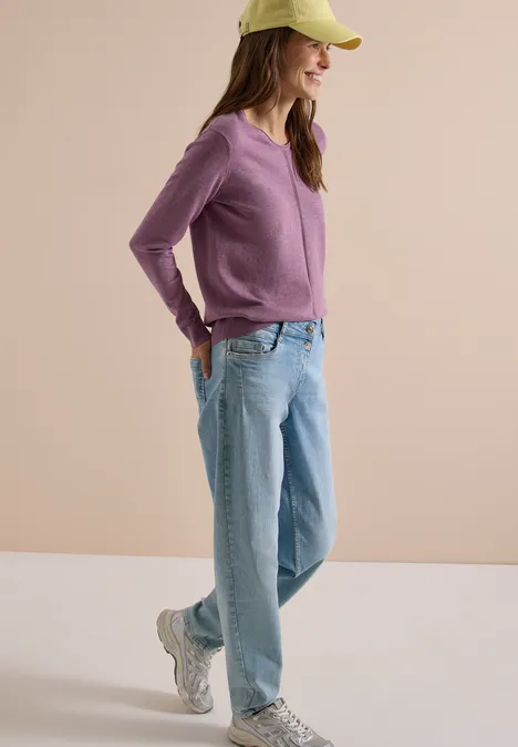 Basic Pullover mit V-Neck in Unifarbe lavender purple melange Eine Frau mit grüner Cap, lila Pullover, hellblauen Jeans und Sneakern lächelt entspannt mit Händen in den Taschen.