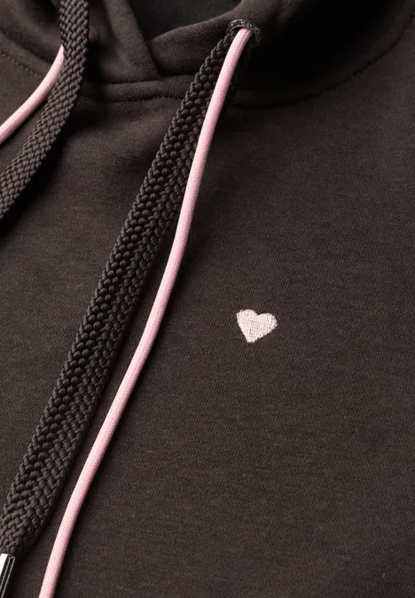 Schwarzer Hoodie mit kleinem weißem Herzmotiv auf der Brust und rosa-schwarzen Kordeln.