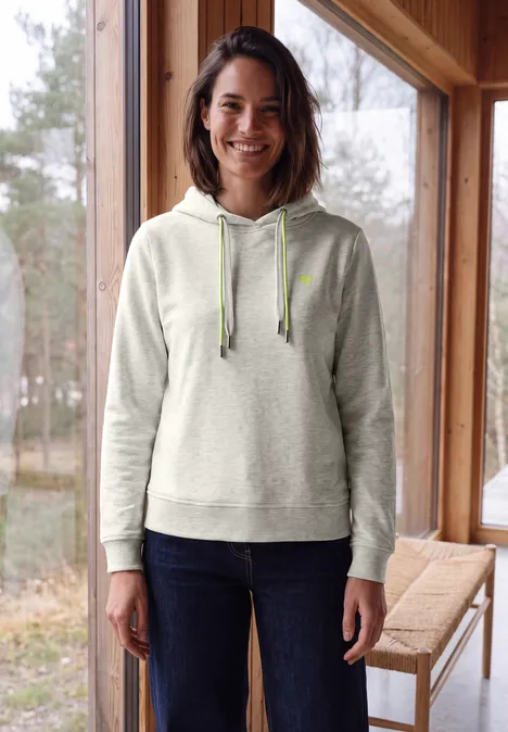 Langarm Sweatshirt mit Kapuze light grey melange Lächelnde Frau in grauem Kapuzenpullover und Jeans steht vor Fenster neben Holztisch