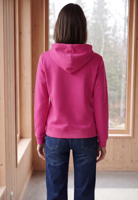 Rückansicht einer Person im pinken Kapuzenpullover, vor einem Fenster in einem Holzraum.