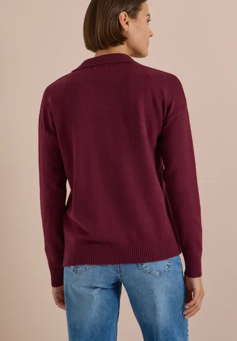 Vue de dos d'une personne portant un pull en maille bordeaux et un jean bleu sur fond uni.