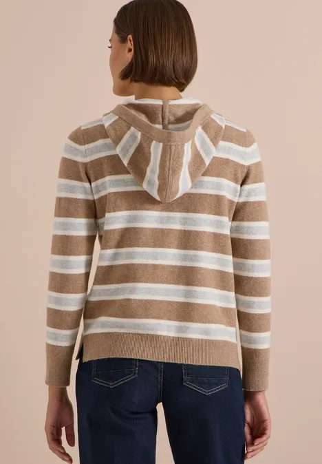 Femme de dos portant un sweat à capuche beige et blanc à rayures, associé à un jean bleu.