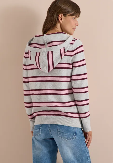 Frau in grauem Kapuzenpullover mit bunten Streifen und Jeans, Rückansicht im Halbprofil.