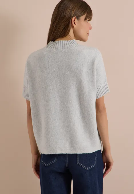 Rückenansicht einer Frau in grauem Kurzarm-Pullover mit hohem Kragen und blauer Jeans.