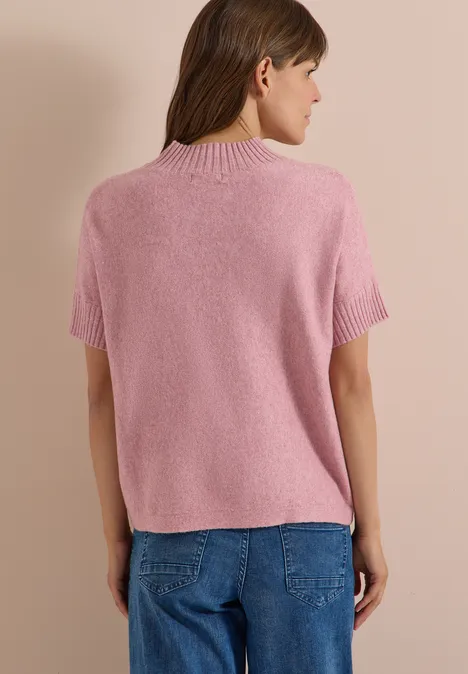 Rückansicht einer Frau in rosa kurzärmligem Pullover und blauer Jeans vor hellbraunem Hintergrund.
