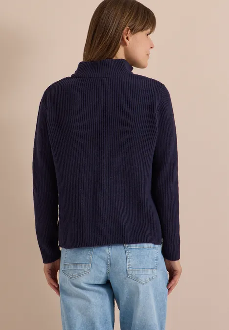 Femme vue de dos en pull en maille bleu marine à col montant et jean clair.
