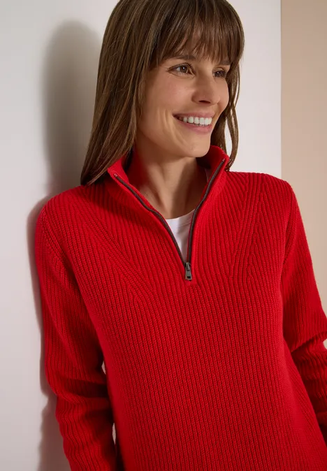 Femme souriante en pull côtelé rouge à demi-fermeture éclair regardant sur le côté
