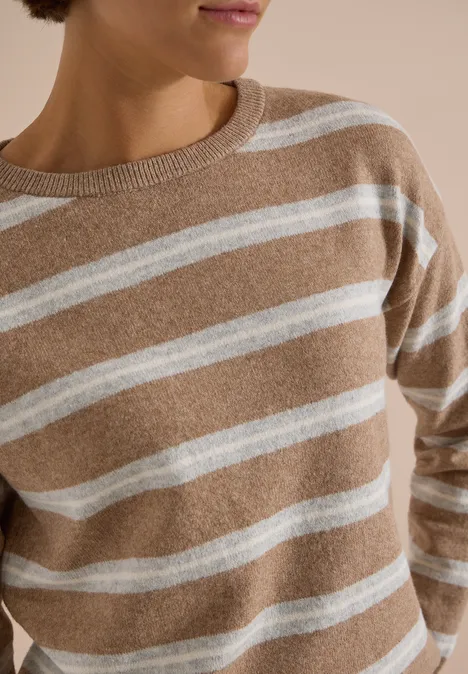 Pull beige à rayures blanches horizontales, porté par une femme, partie supérieure visible.