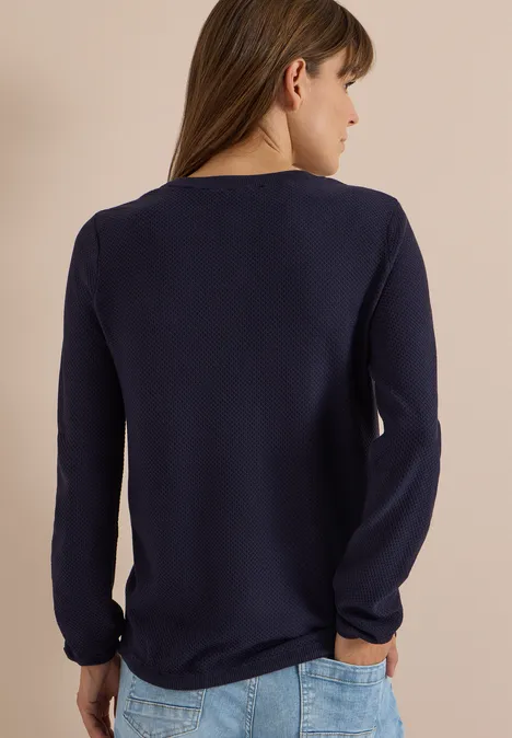 Femme de dos en t-shirt bleu marine à manches longues sur fond clair.