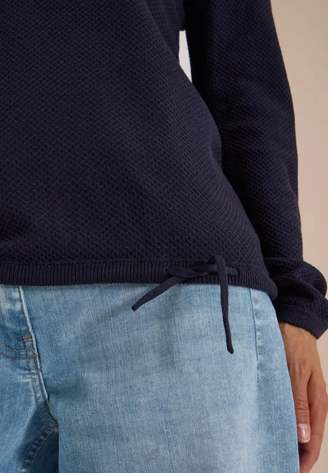 Pull texturé bleu foncé à cordon latéral, associé à un jean bleu clair.