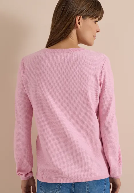 Vue de dos d'une femme portant un pull rose à manches longues et un jean bleu sur fond neutre.