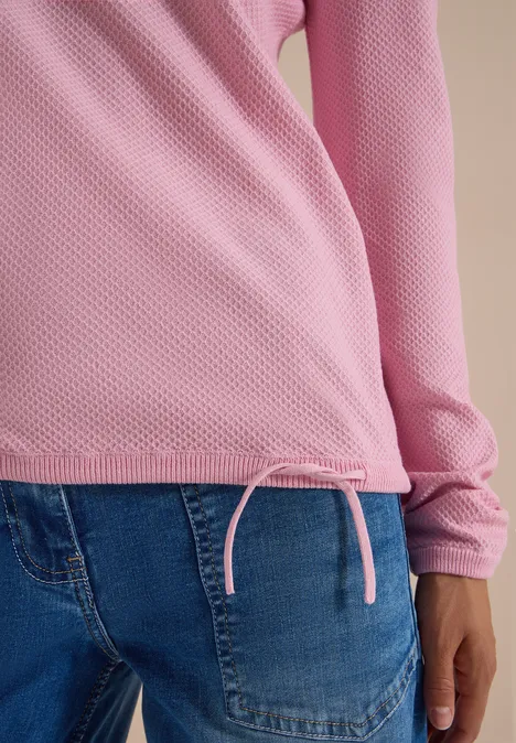 Haut à manches longues rose avec cordon de serrage à la base, associé à un jean bleu.