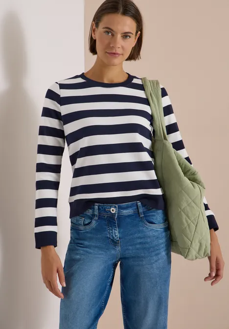 Frau in Jeans und weiß-blau gestreiftem Pullover, trägt grüne Umhängetasche.