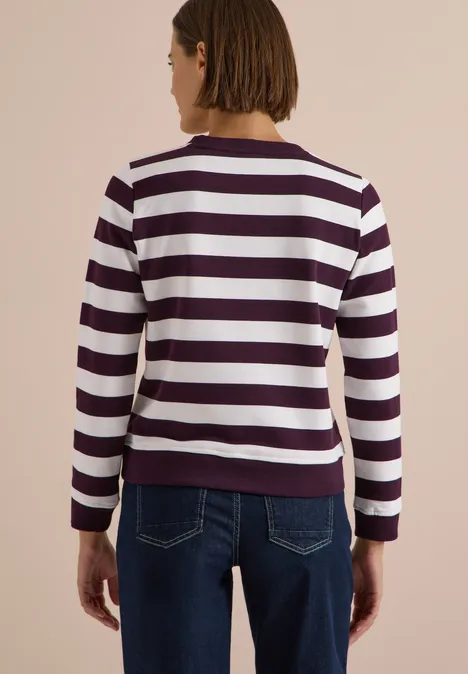 Frau von hinten in gestreiftem Pullover und Jeans vor neutralem Hintergrund.