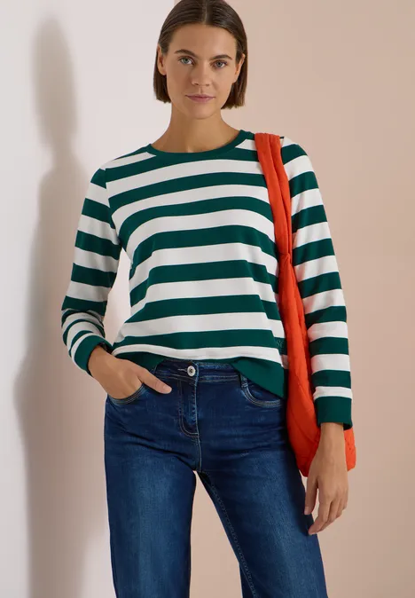 Frau trägt grün-weiß gestreiften Pullover, blaue Jeans und oranger Tasche.