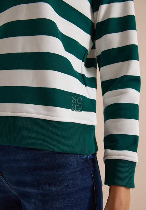Person trägt einen grün-weiß gestreiften Langarm-Pullover und eine blaue Jeans.