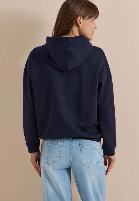Vue de dos d'une femme portant un sweat à capuche bleu marine et un jean clair.