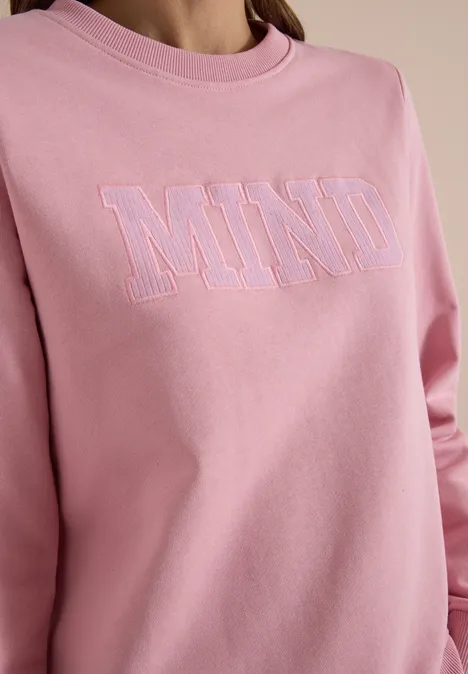 Un sweat rose avec l’inscription 'MIND' en contours pastel.