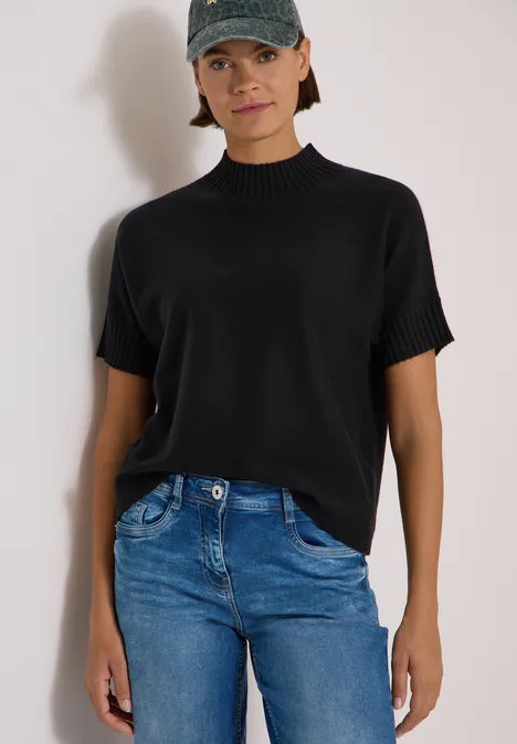 Femme en haut noir à manches courtes et jean bleu sur fond blanc.