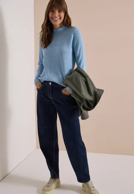 Pull texturé avec des boutons décoratifs easy blue melange Jeune femme souriante en pull bleu clair, jean sombre et baskets blanches, portant une veste verte.