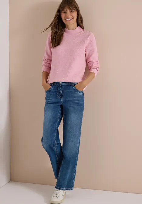 Pull texturé avec boutons décoratifs mellow rose melange Femme en pull rose, jean bleu et baskets blanches devant un fond beige.