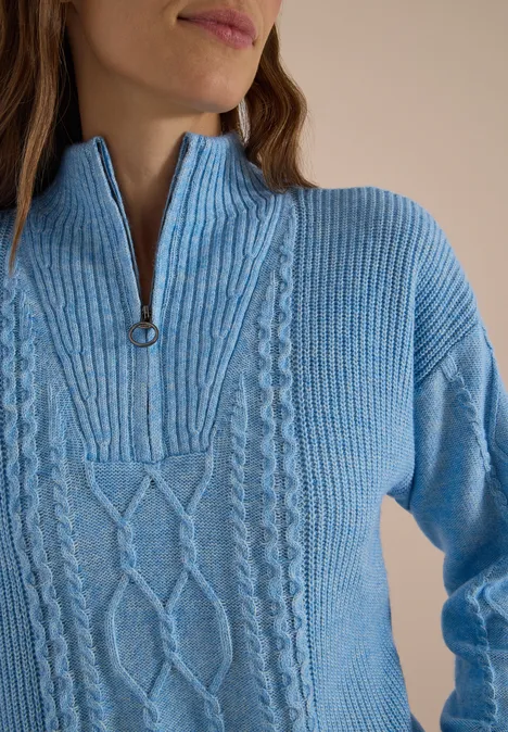 Femme portant un pull en maille bleu clair avec motif torsadé et demi-zip au col.