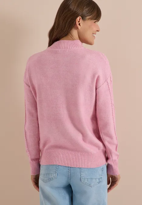 Femme de dos portant un pull rose et un jean bleu clair sur fond beige.