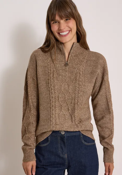 Femme souriante en pull marron à torsades, col montant zippé, style décontracté.