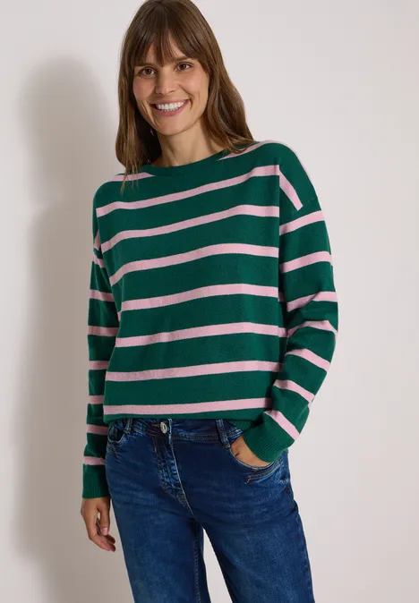Pull à col bateau et rayures dark fir green melange Femme souriante en pull vert à rayures roses et jean.