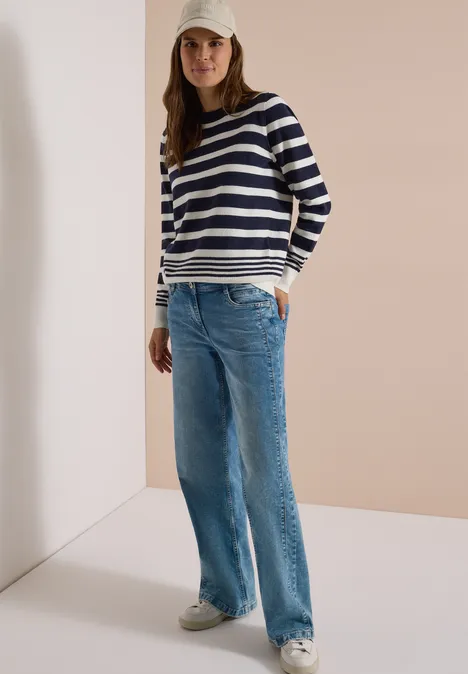 Pull à col rond et à rayures urban dark blue melange Femme décontractée en pull rayé, jean large, baskets et casquette, mains dans les poches.