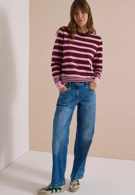 Pull à col rond et rayé red wine melange Femme portant un pull rayé et un jean bleu, debout les mains dans les poches sur un fond neutre.