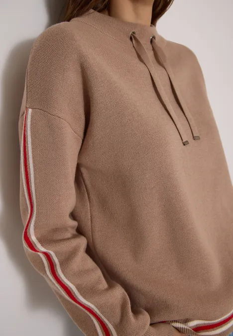 Beiger Pullover mit Kapuze und kontrastierenden roten und weißen Streifen an den Ärmeln.