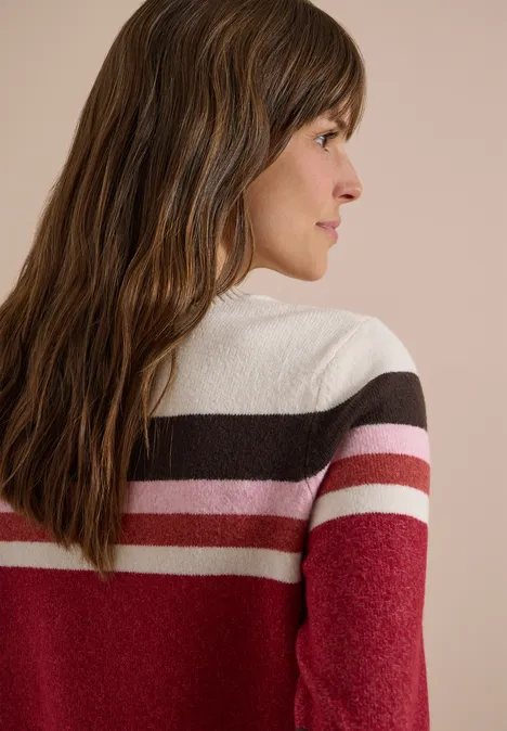 Pull à col rond et rayures rhubarb melange Vue de profil d’une femme aux longs cheveux bruns portant un pull rayé rouge, rose, blanc et marron.